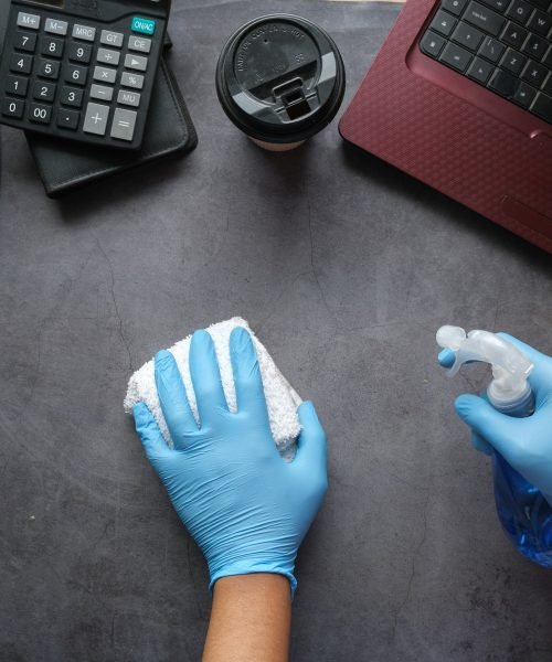 hand-in-blue-rubber-gloves-holding-spray-bottle-cleaning-office-table.jpg